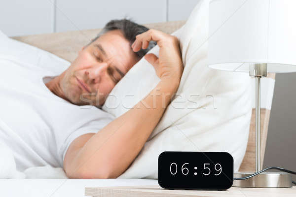 Stock photo: Man On Bed With Clock On Nightstand