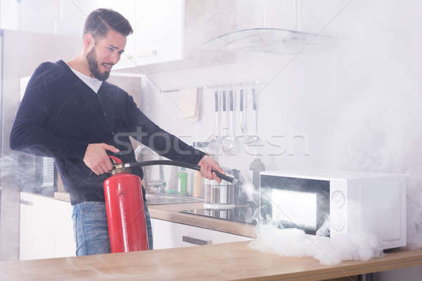 Man Spraying Fire Extinguisher On Microwave Oven Stock photo © AndreyPopov