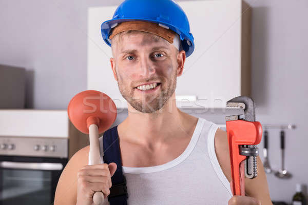 Young Plumber Holding Wrench And Plunger In Kitchen Stock photo © AndreyPopov