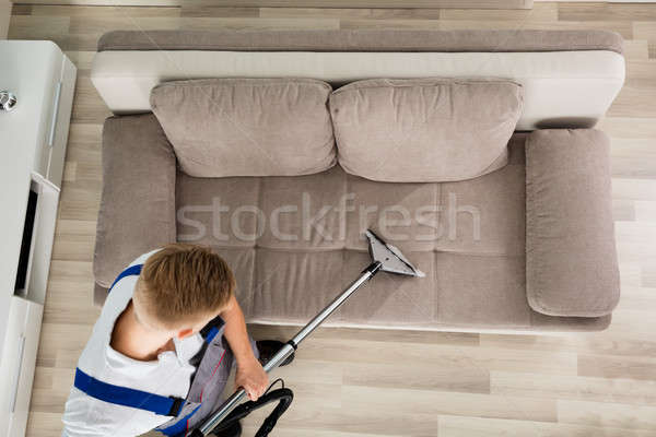 Joven limpia sofá aspiradora vista Foto stock © AndreyPopov