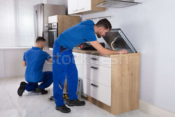Two Men Fixing Induction Stove And Sink Pipe In Kitchen Stock photo © AndreyPopov