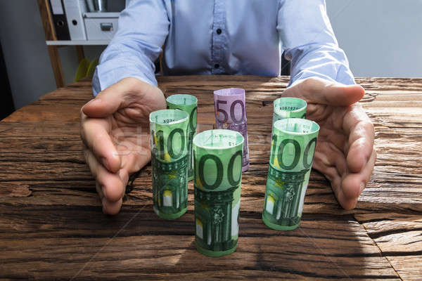 Businessperson's Hand Protecting The Rolled Up Currency Notes Stock photo © AndreyPopov