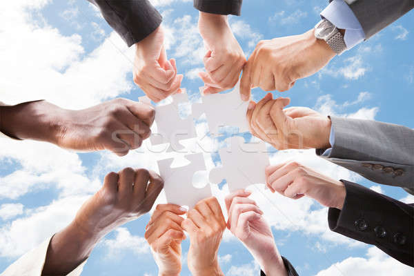 Stock photo: Multiethnic Business People Assembling Jigsaw Puzzle Against Sky