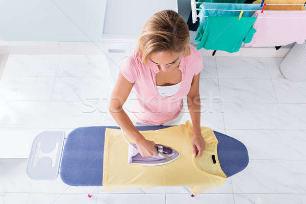 Woman Ironing T Shirt On Ironing Board At Home Stock Photo