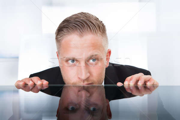 Businessman peering furtively over the top of his desk Stock photo © AndreyPopov