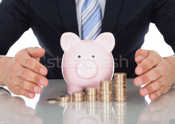 Stock photo: Businessman Sheltering Coins And Piggybank At Desk