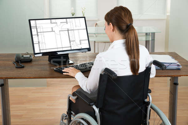 Stock photo: Architect On Wheelchair Looking At Blueprint On Computer