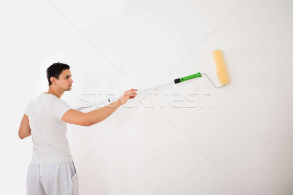 Stock photo: Man Using Paint Roller On White Wall