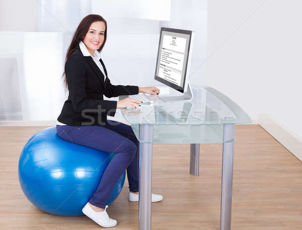 Businesswoman Using Computer While Sitting On Pilates Ball Stock