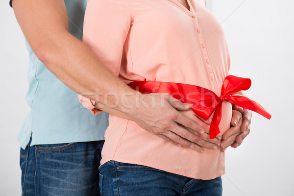Man Embracing Pregnant Woman's Belly Tied With Red Ribbon Stock photo © AndreyPopov