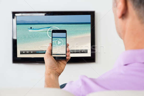 Man With Smartphone Connected To A TV Watching Video Stock photo © AndreyPopov