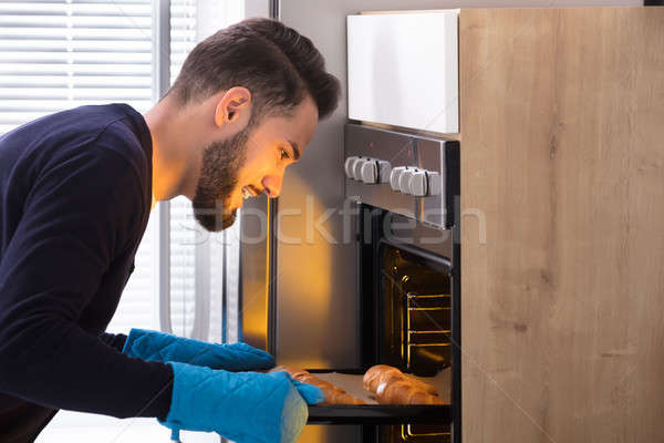 Smiling Young Man Taking Out Tray Of Croissants From Oven Stock photo © AndreyPopov