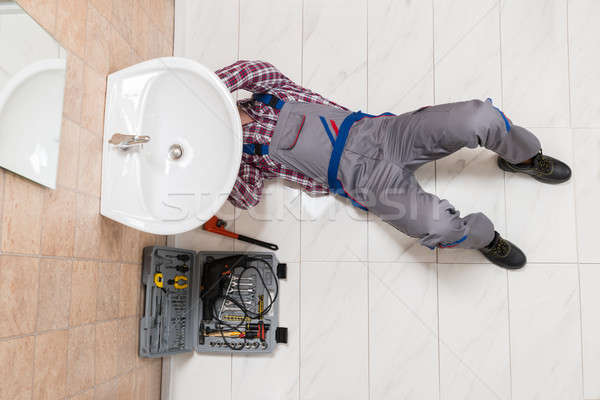 Male Plumber Lying On Floor Repairing Sink In Bathroom Stock photo © AndreyPopov