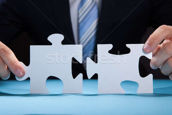 Businessman Joining Puzzle Pieces At Desk Stock photo © AndreyPopov