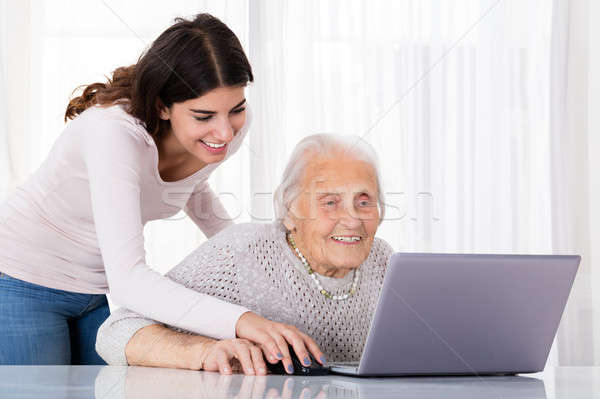 Dos sonriendo mujeres usando la computadora portátil ayudar Foto stock © AndreyPopov