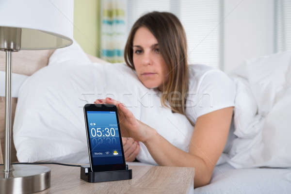 Woman On Bed Snoozing Alarm On Mobile Phone Stock photo © AndreyPopov
