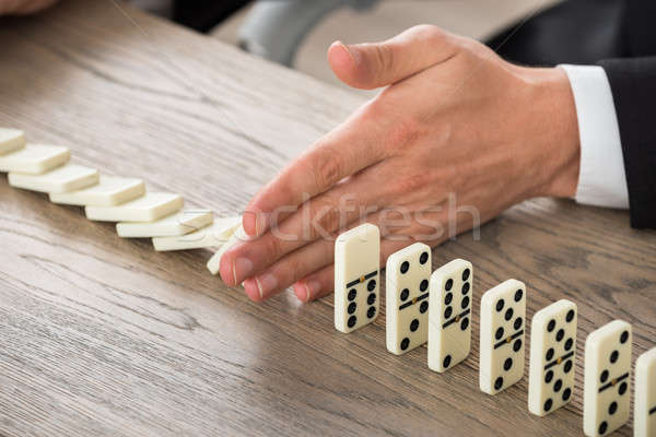 Businessman Hand Stopping Dominoes From Falling On Desk Stock photo © AndreyPopov