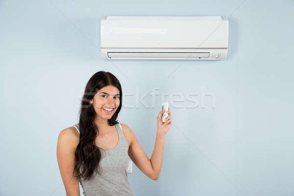 Woman With Remote Control In Front Of Air Conditioner Stock photo © AndreyPopov