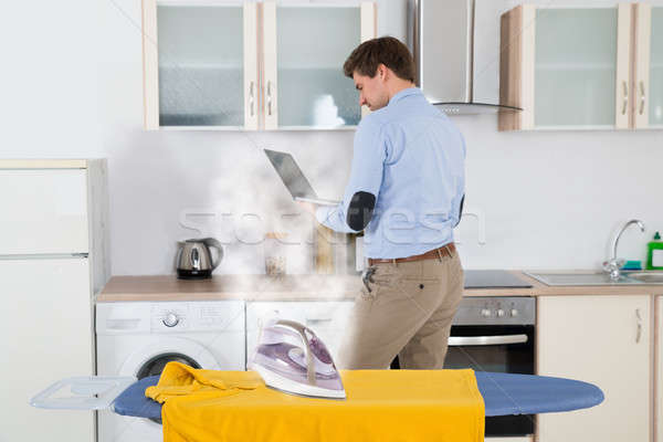 Stock photo: Electric Iron On Cloth While Man With Laptop