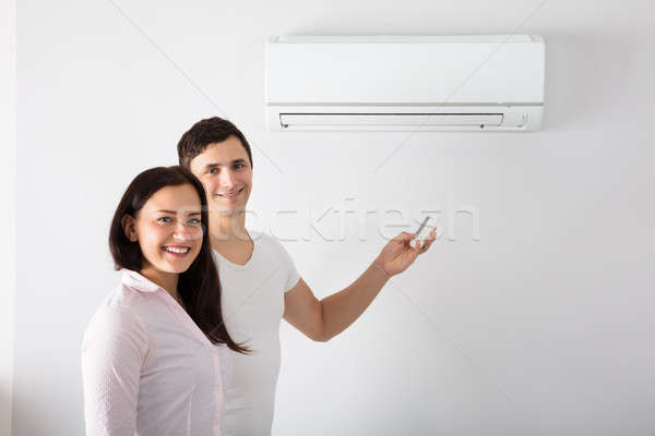 Stock photo: Couple Adjusting Temperature Of Air Conditioner
