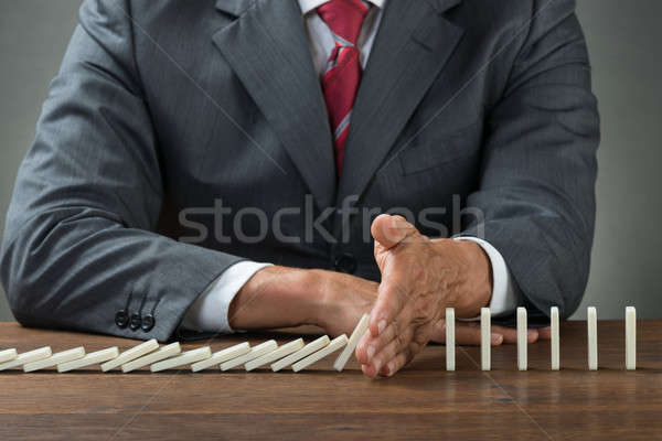 Businessman Stopping Dominoes Falling On Wooden Desk Stock photo © AndreyPopov