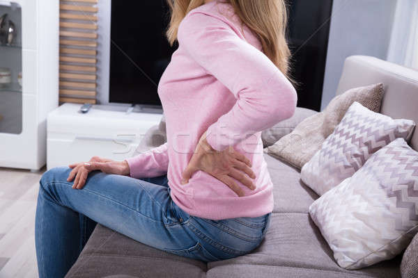 Femeie matura dureri de spate şedinţei canapea acasă Imagine de stoc © AndreyPopov