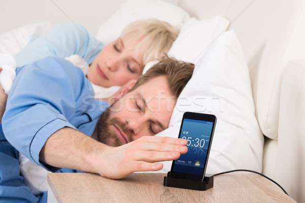 Man On Bed Snoozing Alarm Clock On Cell Phone Stock photo © AndreyPopov