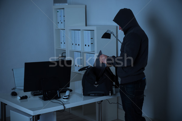Burglar Putting Laptop Into Bag At Desk In Office Stock photo © AndreyPopov