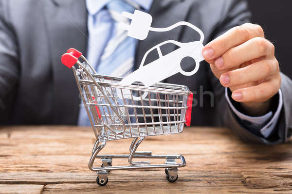 Businessman Holding Electric Paper Car Over Shopping Cart Stock photo © AndreyPopov