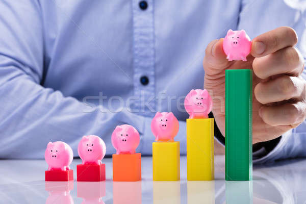 Stock photo: Businessperson Placing Piggy Bank On Top Of Business Graph