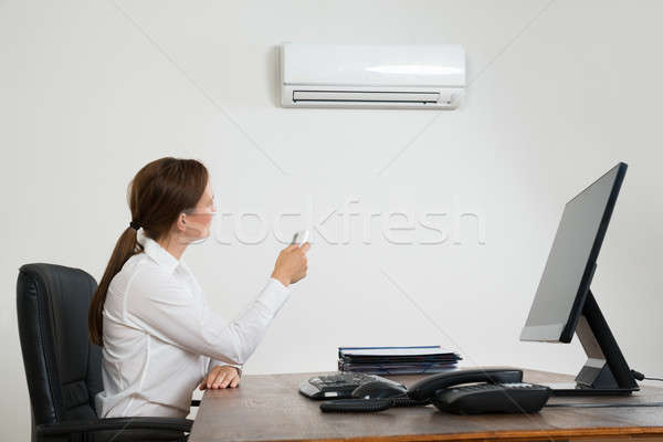 Businesswoman Using Remote Control In Front Of Air Conditioner Stock photo © AndreyPopov