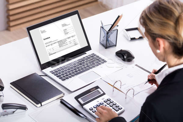 Stock photo: Businesswoman Calculating Invoice Using Calculator And Laptop