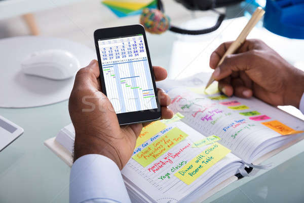 Stock photo: Businessman Holding Cellphone Writing Schedule In Diary