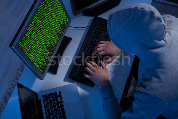 Hacker In Hooded Jacket Using Computer At Table Stock photo © AndreyPopov
