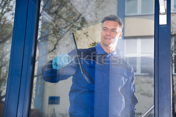 Stock photo: Male Worker Cleaning Glass With Squeegee