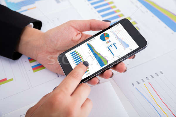 Businesswoman Analyzing Financial Graphs Using Smartphone Stock photo © AndreyPopov