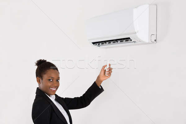 Stock photo: Businesswoman Operating Air Conditioner In Office