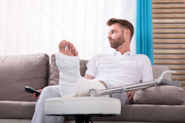 Człowiek złamana noga posiedzenia sofa młody człowiek Zdjęcia stock © AndreyPopov