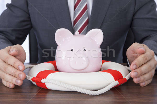 Businessman Sheltering Piggybank With Lifebelt At Desk Stock photo © AndreyPopov