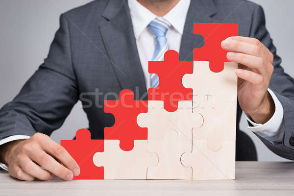 Stock photo: Businessman Holding Red Jigsaw Graph On Table