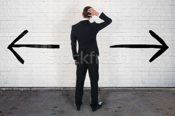 Confused Businessman Looking At Opposite Arrow Signs On Wall Stock photo © AndreyPopov