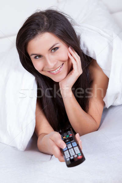 Woman lying in bed with a remote control Stock photo © AndreyPopov