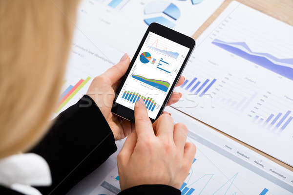 Businesswoman Analyzing Graph Using Mobilephone Stock photo © AndreyPopov