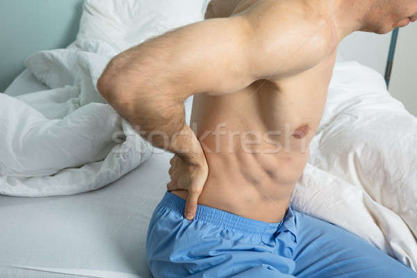 Hombre dolor de espalda primer plano sesión cama sufrimiento Foto stock © AndreyPopov