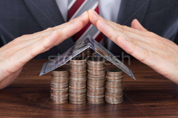 Businessman Sheltering Coins And Banknote In House Shape Stock photo © AndreyPopov