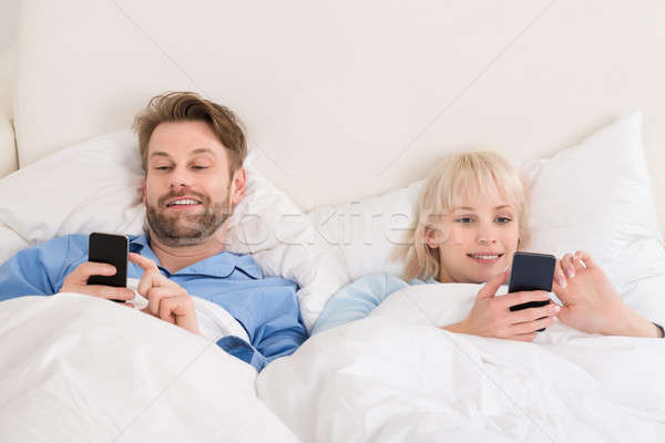 Happy Couple Using Cellphones Lying On Bed Stock photo © AndreyPopov