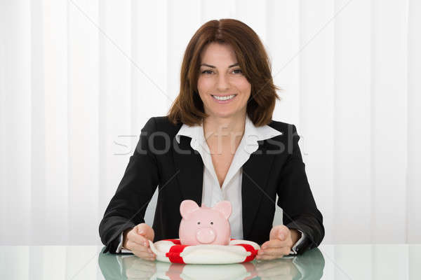 Businesswoman Sheltering Piggybank With Lifebelt Stock photo © AndreyPopov