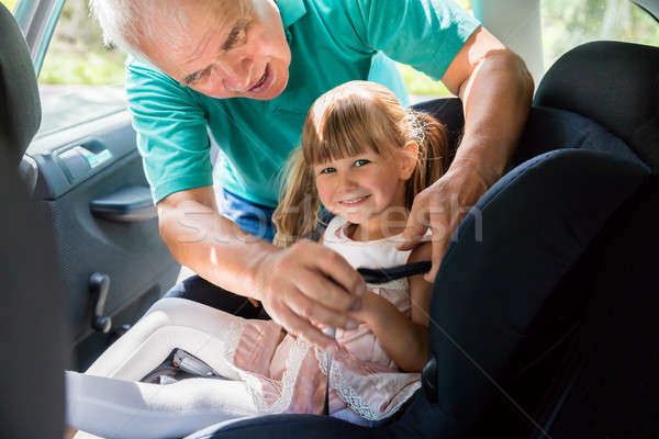 Stock photo: Grandfather Buckling Up On Granddaughter In Car Safety Seat