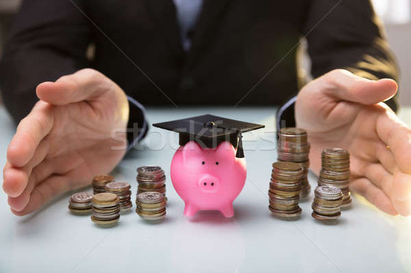 Businessperson Protecting Piggy Bank Wearing Graduation Hat Stock photo © AndreyPopov
