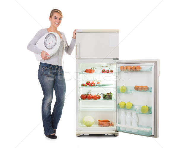 Woman Holding Weighing Scale While Standing By Refrigerator Stock photo © AndreyPopov